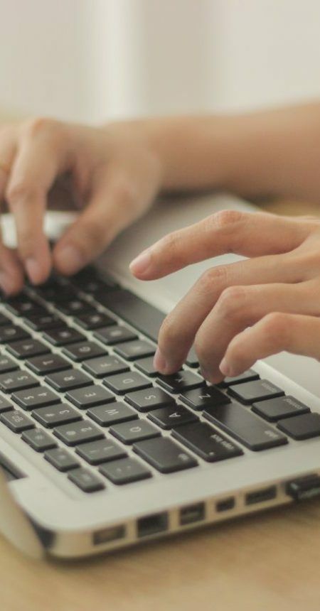 person-sitting-in-front-of-desk-and-typing-on-the-keyboard-of-the-laptop person-sitting-in-front-of-desk-and-typing-on-the-keyboard-of-the-laptop